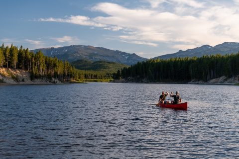 Group of people canoeing on a serene lake with forest and mountains in the backdrop in Sheridan, Wyoming.