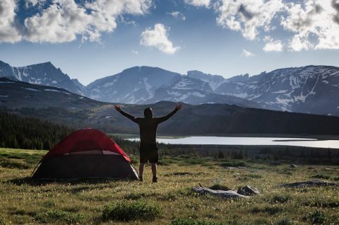 A person rejoices at dawn near a campsite with a mountain lake backdrop, a top thing to do for outdoor enthusiasts in Sheridan, Wyoming.
