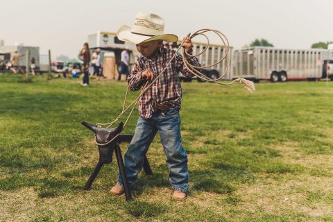 Young boy in cowboy attire practicing roping on a metal steer dummy at Don King Days event.