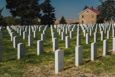 Rows of uniform white headstones in a national cemetery, with a historic building in the background under a clear sky.