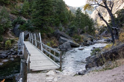 A wooden bridge crosses the serene Tongue River Canyon, surrounded by rugged terrain and fall colors, a top choice for day hikes near Sheridan.