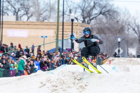 A skier in black gear and yellow skis catches air during a skijoring race in Sheridan, WY.