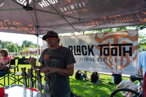Vendor representing Black Tooth Brewing Co. at Sheridan Brewfest, engaging with attendees in front of a branded tent.