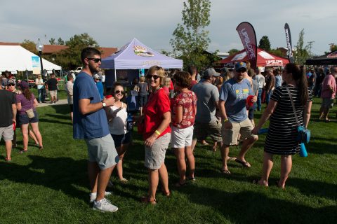 Attendees walking around and socializing at the Sheridan Brewfest, surrounded by brewery stands and green trees.