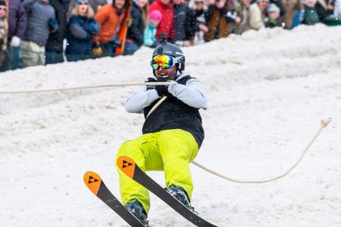 A skier in bright yellow pants and dark jacket performs skijoring, being pulled on snow by a horse, a thrilling winter sport in Sheridan, WY.