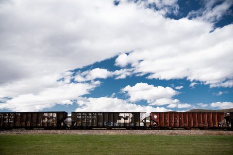 A train with graffiti-covered cars sits stationary on tracks in Clearmont, Wyoming, against a backdrop of a blue sky with white clouds.