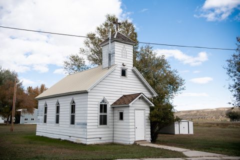 White, small-town church with a steeple and a separate outhouse in Clearmont, Wyoming.