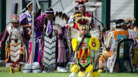 Children in colorful traditional attire performing at a First People's Pow Wow event.