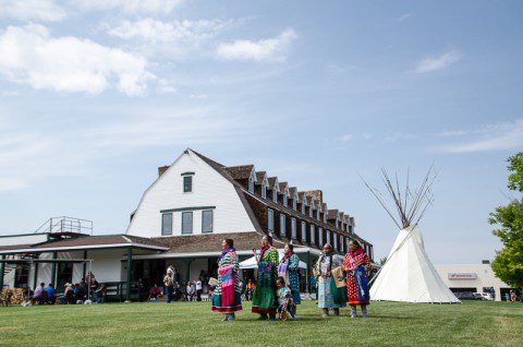 Participants in vibrant attire at a Native American powwow with the Historic Sheridan Inn in the backdrop.
